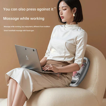 Woman using a handheld massage device while working on a laptop.
